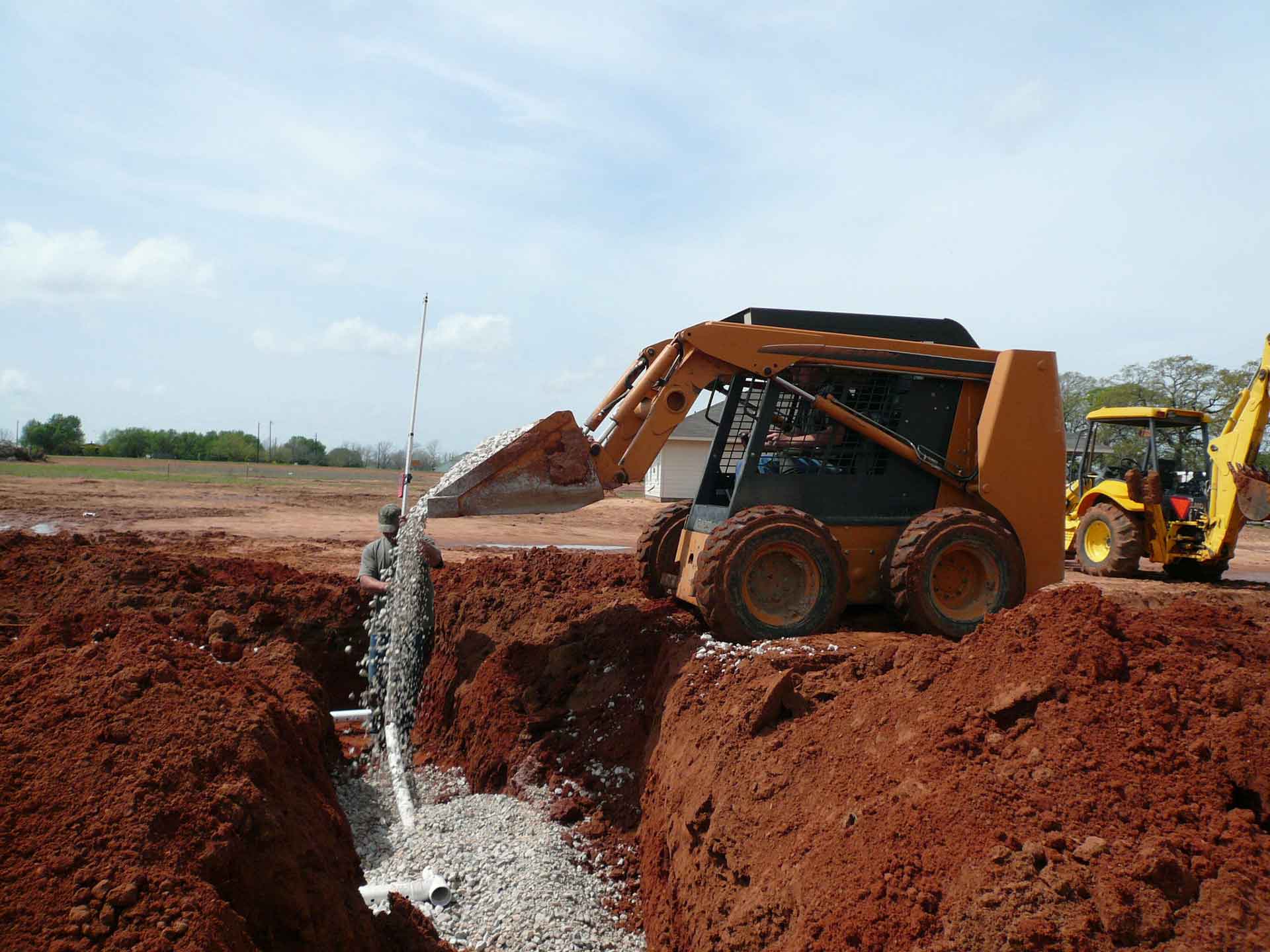Men using a tractor to fill in a ditch dug for a septic system with gravel